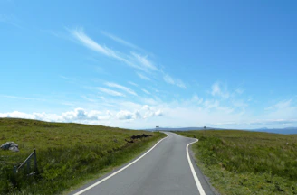 A scenic view of a winding outback road stretching into the horizon under a vast blue sky.