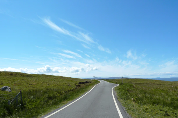 A scenic view of a winding outback road stretching into the horizon under a vast blue sky.