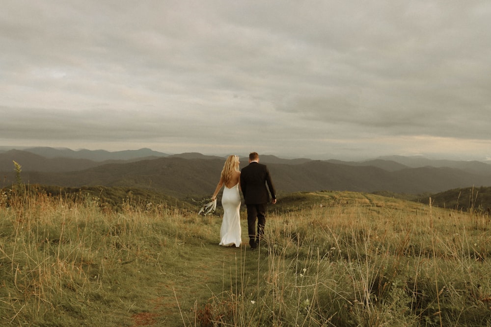 Un hombre y una mujer parados en un campo de hierba alta con colinas en el fondo