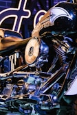 A close-up view of a motorcycle, showcasing the intricate details of its chrome engine and parts. The Harley-Davidson branding is visible on the fuel tank, and the lighting is predominantly blue with highlights of neon, adding a modern and sleek look.