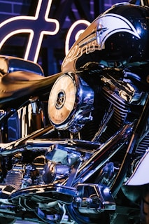 A close-up view of a motorcycle, showcasing the intricate details of its chrome engine and parts. The Harley-Davidson branding is visible on the fuel tank, and the lighting is predominantly blue with highlights of neon, adding a modern and sleek look.