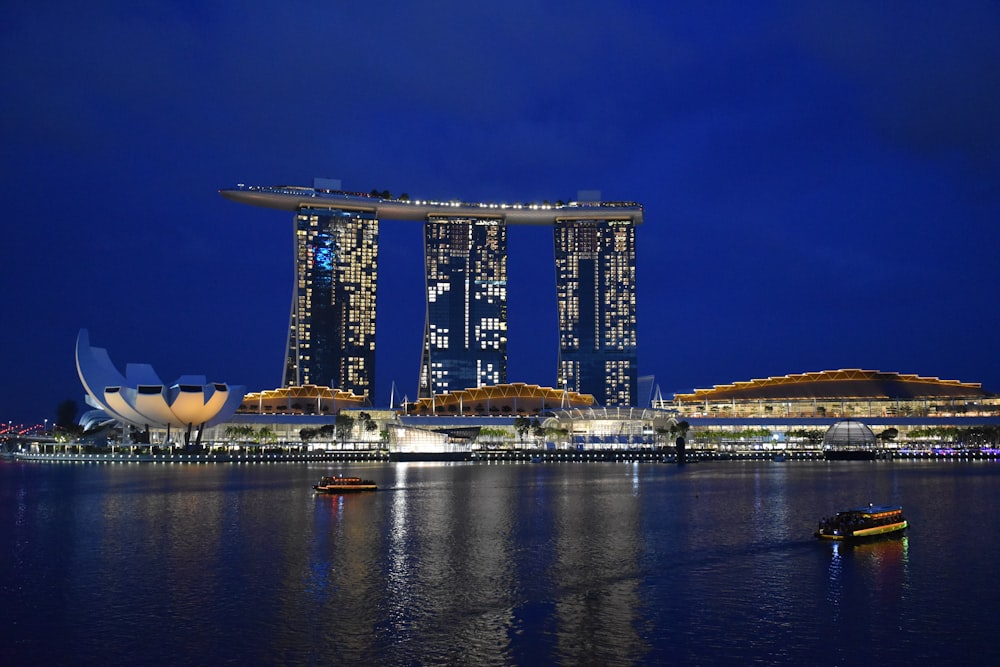 a large building with a large glass window next to a body of water with Marina Bay Sands in the background