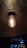 A single exposed incandescent light bulb hanging from a ceiling fixture, casting a warm glow. The background is dimly lit, highlighting the bulb's filament and creating a contrast between the illuminated bulb and the dark, industrial setting.