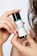 A hand holds a small bottle labeled with skincare information, while curly hair is visible in the background. The label mentions AHA, BHA, and PHA, indicating its use as a toner for skin care.