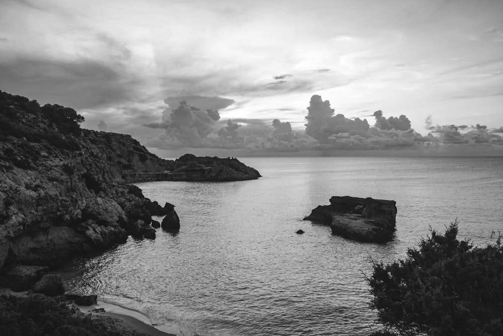 a rocky beach with a body of water and trees on the side