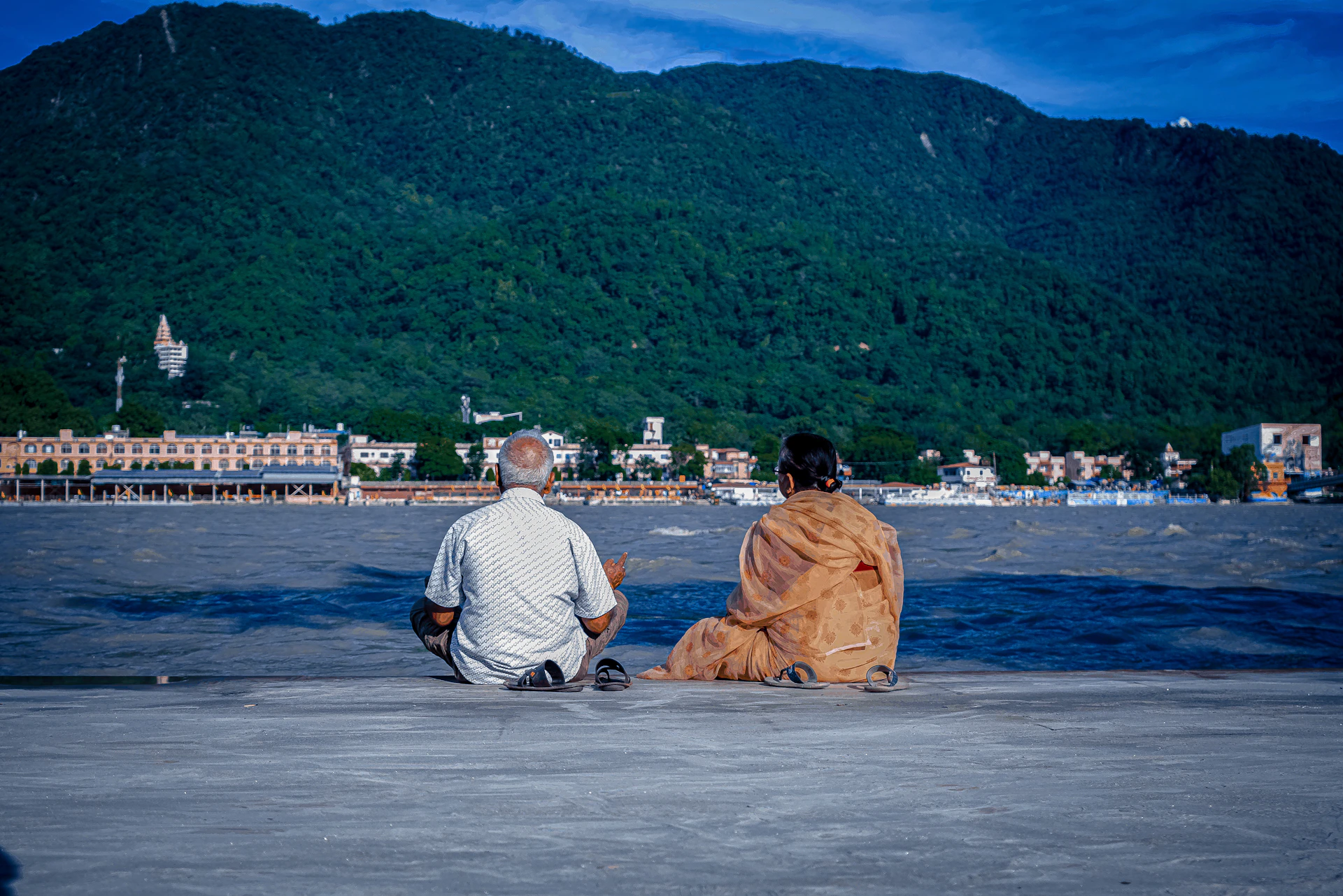 a man and woman sitting on a beach looking at a mountain