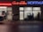 A storefront at night featuring two adjacent businesses. On the left, a hair studio with signs on the door and windows. On the right, a beverage store named 'Getränke Hoffmann' with illuminated red and blue signage. The sidewalk is covered with scattered leaves, and the reflections on wet pavement suggest recent rain.
