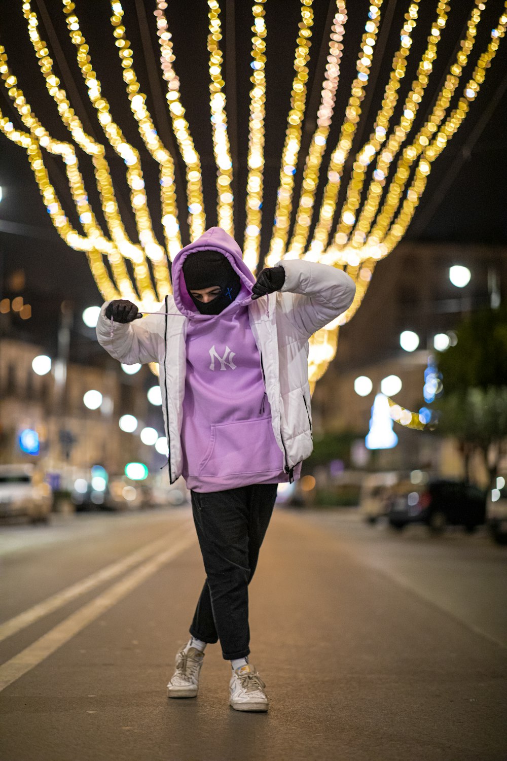 a person wearing a pink jacket and standing on a street with lights