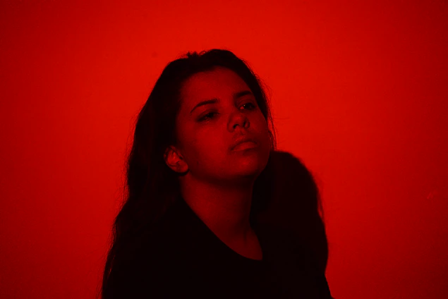 A moody, cinematic portrait of Gwen Lilly bathed in soft shadows with a dark red and gold color palette.