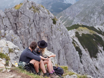 a man and woman sitting on a rock with a mountain in the background