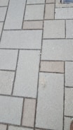 Concrete paving stones arranged in a rectangular pattern, with a mix of light and dark shades. The surface appears slightly rough and weathered.