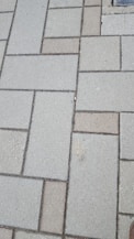 Concrete paving stones arranged in a rectangular pattern, with a mix of light and dark shades. The surface appears slightly rough and weathered.