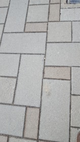 Concrete paving stones arranged in a rectangular pattern, with a mix of light and dark shades. The surface appears slightly rough and weathered.
