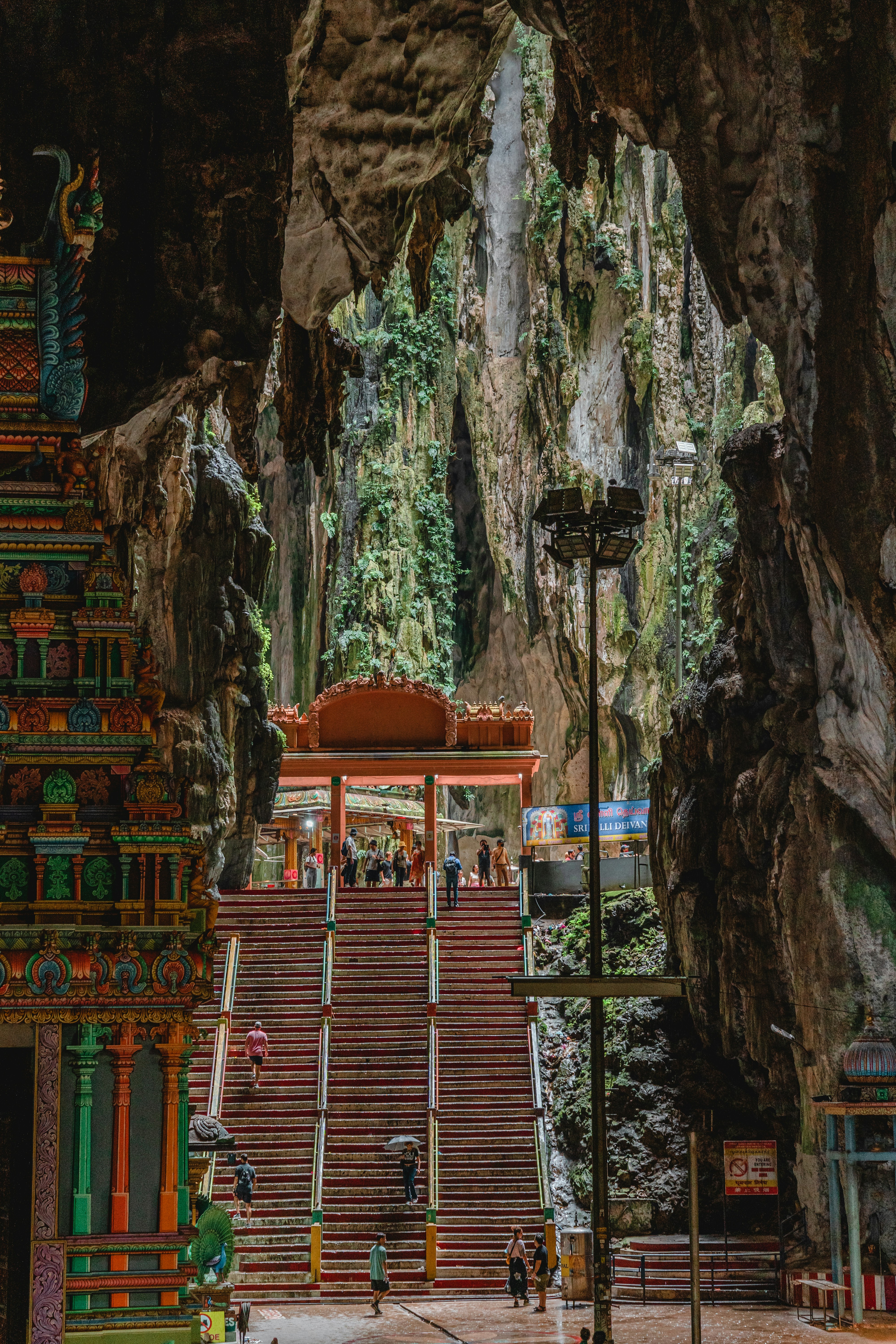 a large stone building with a large archway with Batu Caves in the background