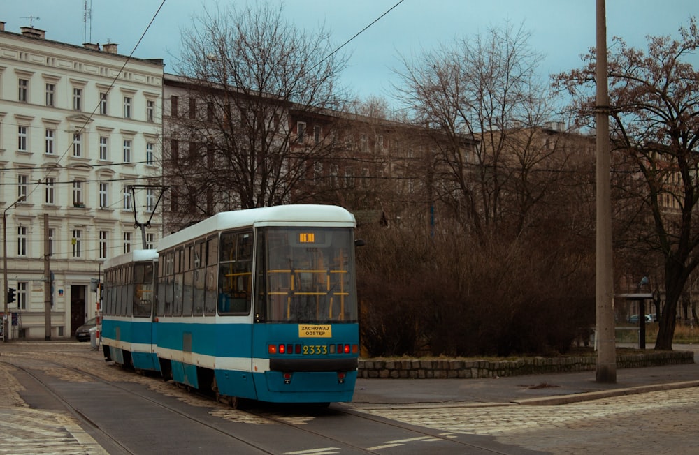 a blue and white trolley on a street with buildings on either side