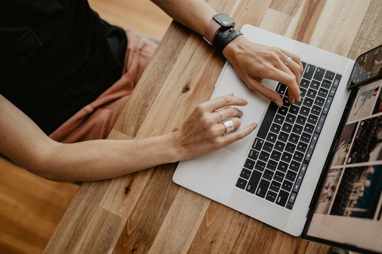 Close-up of hands typing on a laptop keyboard at a wooden desk