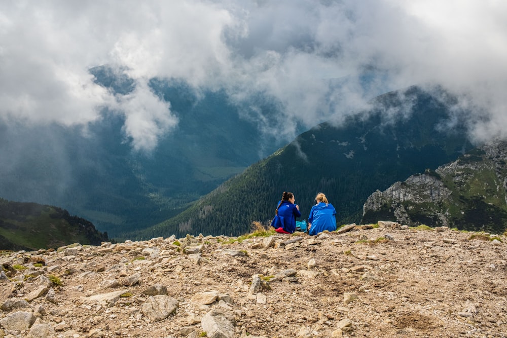 two people sitting on a rocky hill