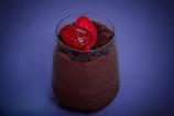 Close-up of a creamy chocolate mousse topped with fresh raspberries on a rustic wooden table.