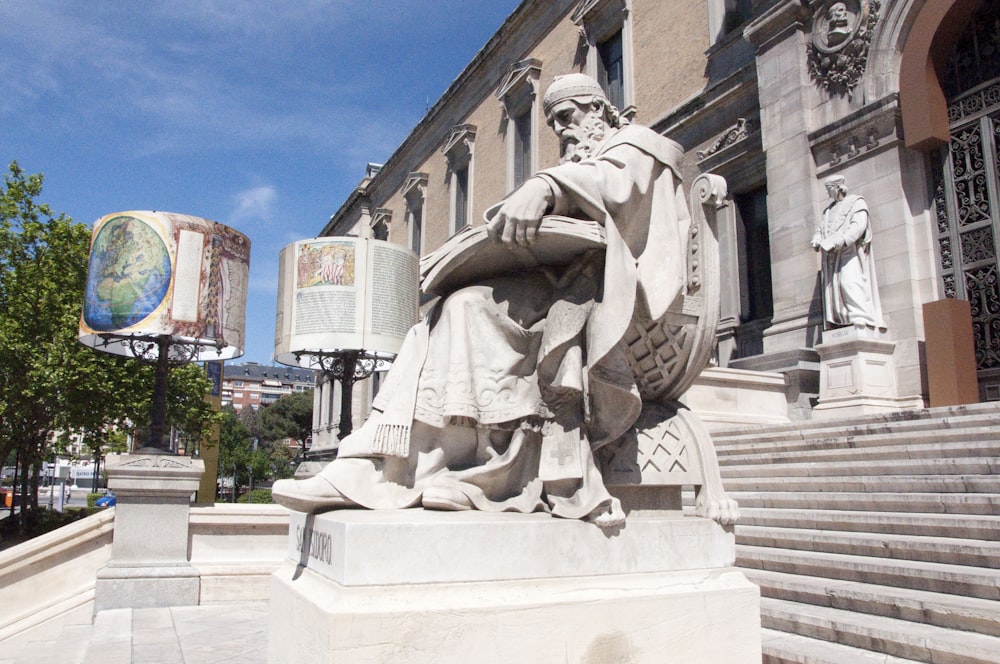 a statue of a person sitting on a stone pedestal in front of a building