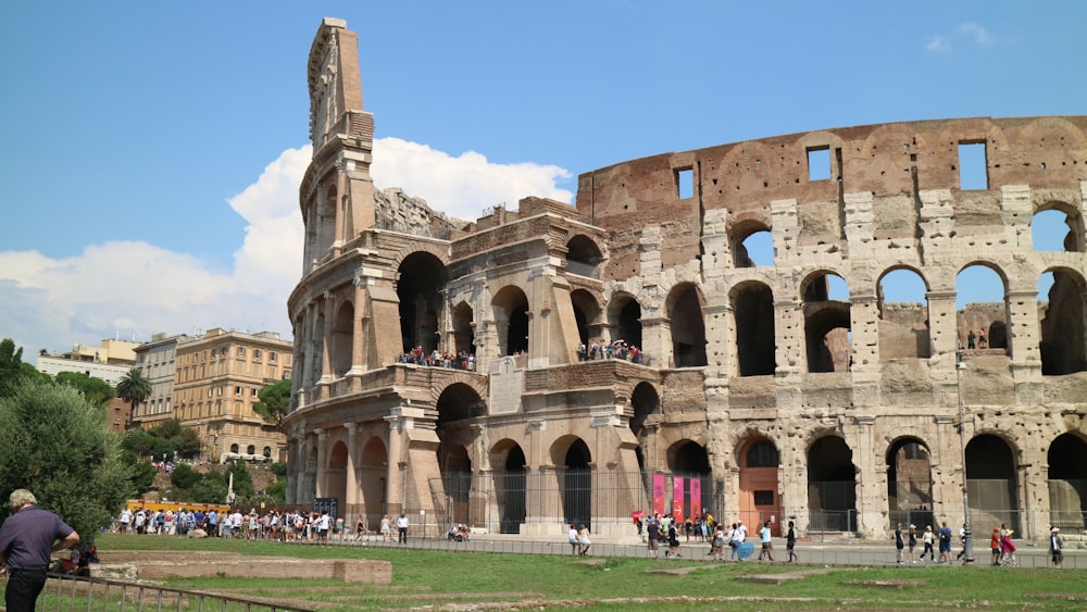 a large stone building with a group of people in front of it with Colosseum in the background