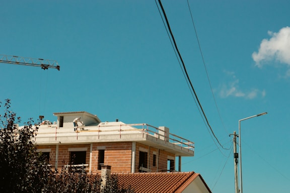 A construction worker inspecting a roof with tools in hand under a clear blue sky.