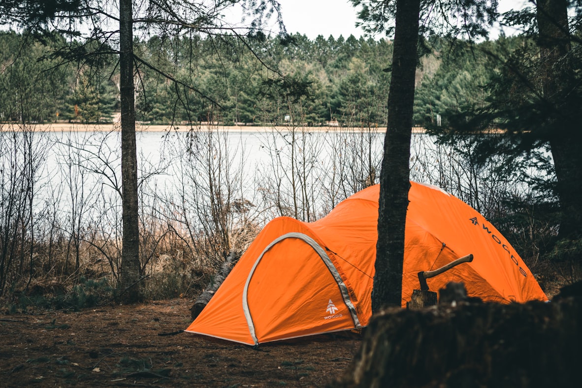 A small one-person tent pitched on a flat rock by a still mountain lake, the most efficient possible accommodation