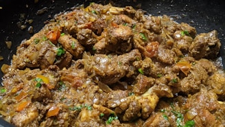 A close-up view of cooked meat pieces mixed with chopped onions, tomatoes, and herbs. The dish appears to be richly spiced and garnished with fresh green cilantro.