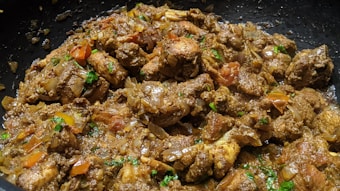 A close-up view of cooked meat pieces mixed with chopped onions, tomatoes, and herbs. The dish appears to be richly spiced and garnished with fresh green cilantro.
