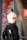 A person with light blonde hair and glasses is wearing a black jacket with a logo featuring a footprint and the letters 'ics'. They are standing in front of an artistic background featuring abstract red branches or coral against a muted backdrop, with a metal or industrial object partially visible on one side.