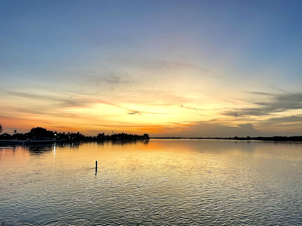 a body of water with trees and a sunset in the background