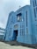 A large, blue-painted church with tall vertical windows and art deco architectural elements. The structure features a cross on top and a religious statue set into a niche above the main entrance. The building has a symmetrical facade with geometric designs.