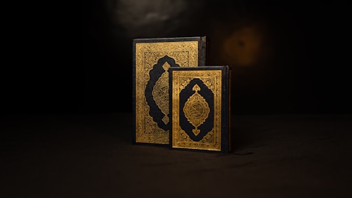 Two ornate books with intricate gold and black covers are prominently displayed. The books are positioned against a dark background, highlighting their detailed patterns and rich colors.