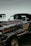 A close-up view of a shiny, chrome-plated vintage car against a waterfront backdrop. The car features an exposed engine with intricate detailing and polished metal components. The background shows calm waters and a pier with support pillars extending into the water.