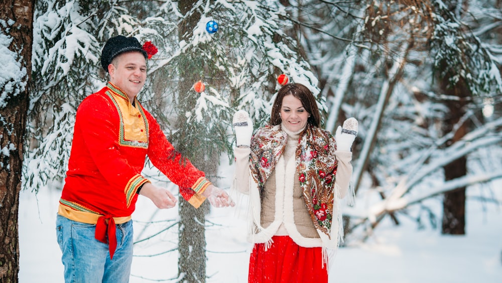 a man and woman holding hands in front of a snow covered tree