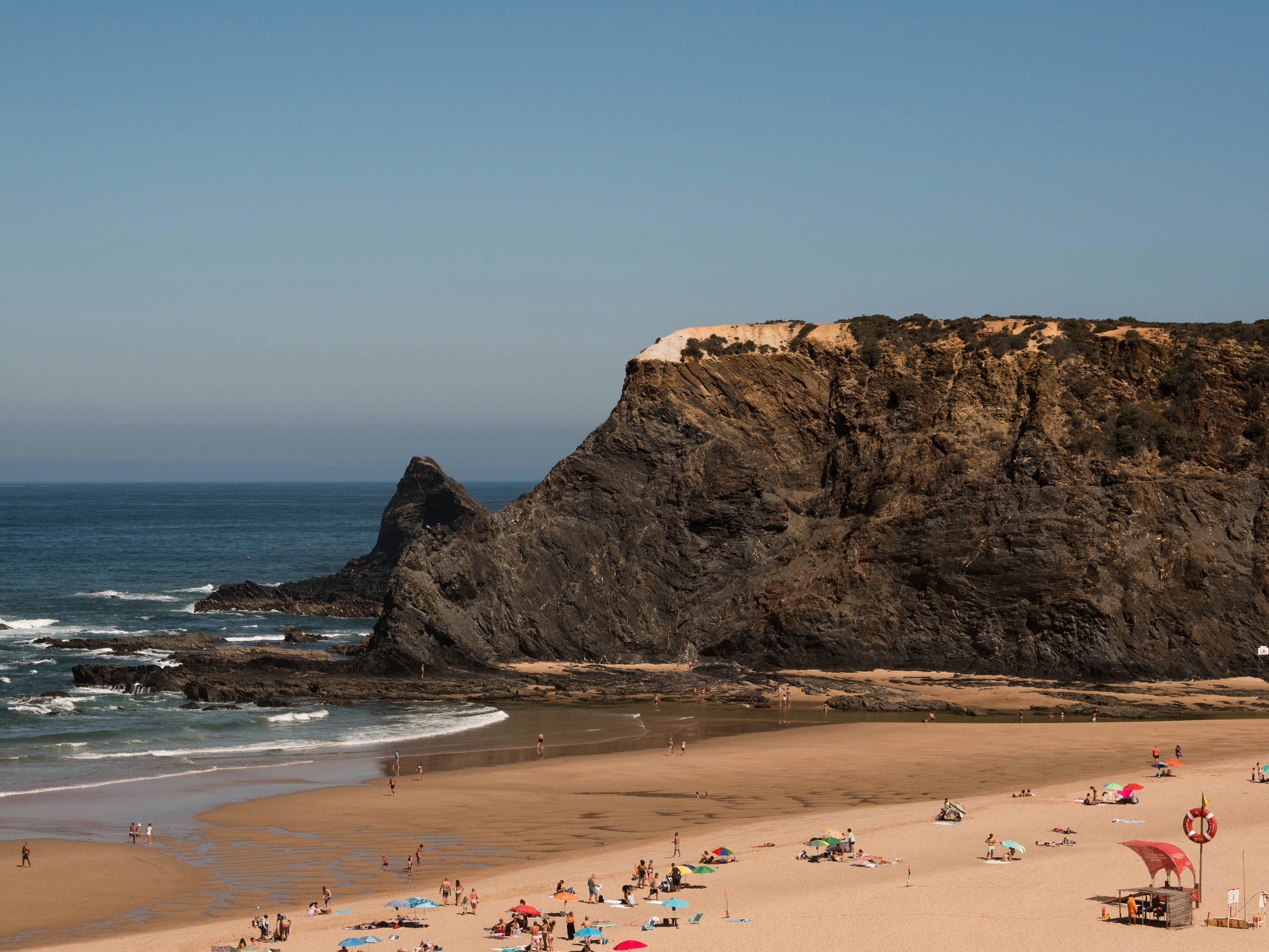 Una playa con gente y una gran roca al fondo