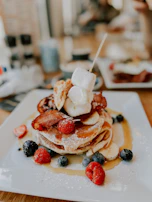 A stack of fluffy pancakes topped with whipped cream and a drizzle of maple syrup, perfect for late-night cravings.