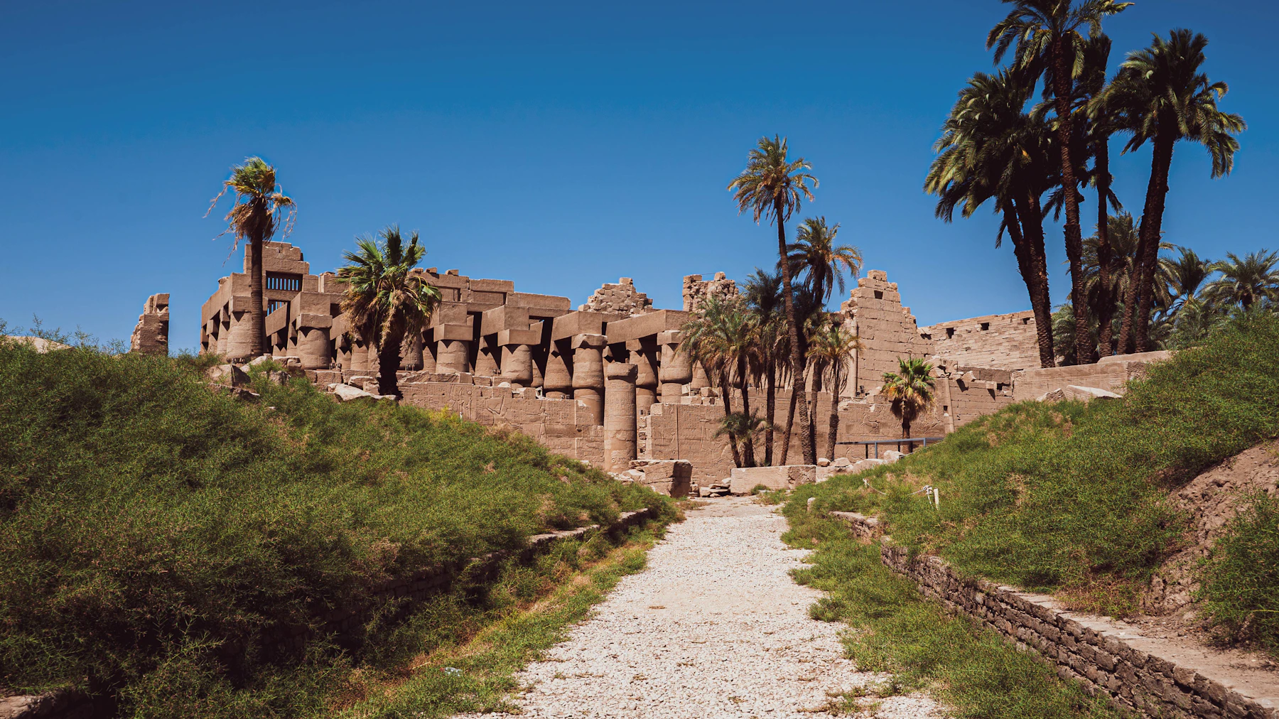 A gravel walkway leads between stone structures at Karnak.