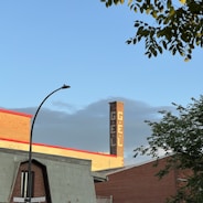 A red brick industrial building is visible with a tall chimney featuring white lettering spelling 'GÉL'. In the foreground, there is a street sign at the intersection of Rachel St and Saint-André, along with some tree branches. The sky is clear with a hint of clouds.