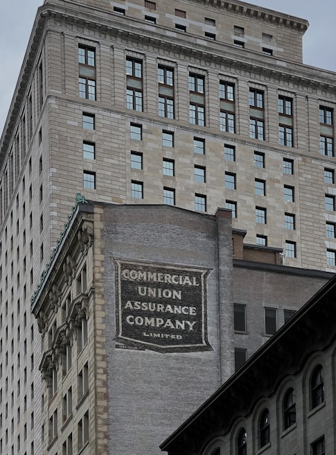 A tall building with an intricate architectural design and a large advertisement painted on one of its walls for the Commercial Union Assurance Company. The facade features numerous windows in a symmetrical pattern, and the structure has a historic, early 20th-century appearance.