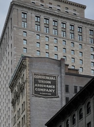 A tall building with an intricate architectural design and a large advertisement painted on one of its walls for the Commercial Union Assurance Company. The facade features numerous windows in a symmetrical pattern, and the structure has a historic, early 20th-century appearance.
