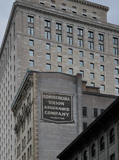 A tall building with an intricate architectural design and a large advertisement painted on one of its walls for the Commercial Union Assurance Company. The facade features numerous windows in a symmetrical pattern, and the structure has a historic, early 20th-century appearance.