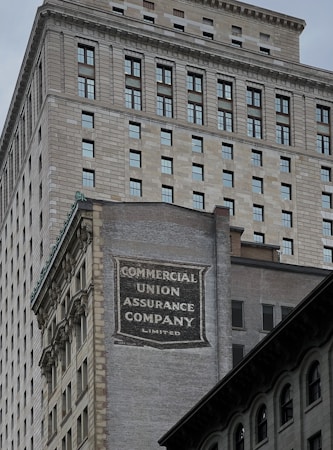 A tall building with an intricate architectural design and a large advertisement painted on one of its walls for the Commercial Union Assurance Company. The facade features numerous windows in a symmetrical pattern, and the structure has a historic, early 20th-century appearance.