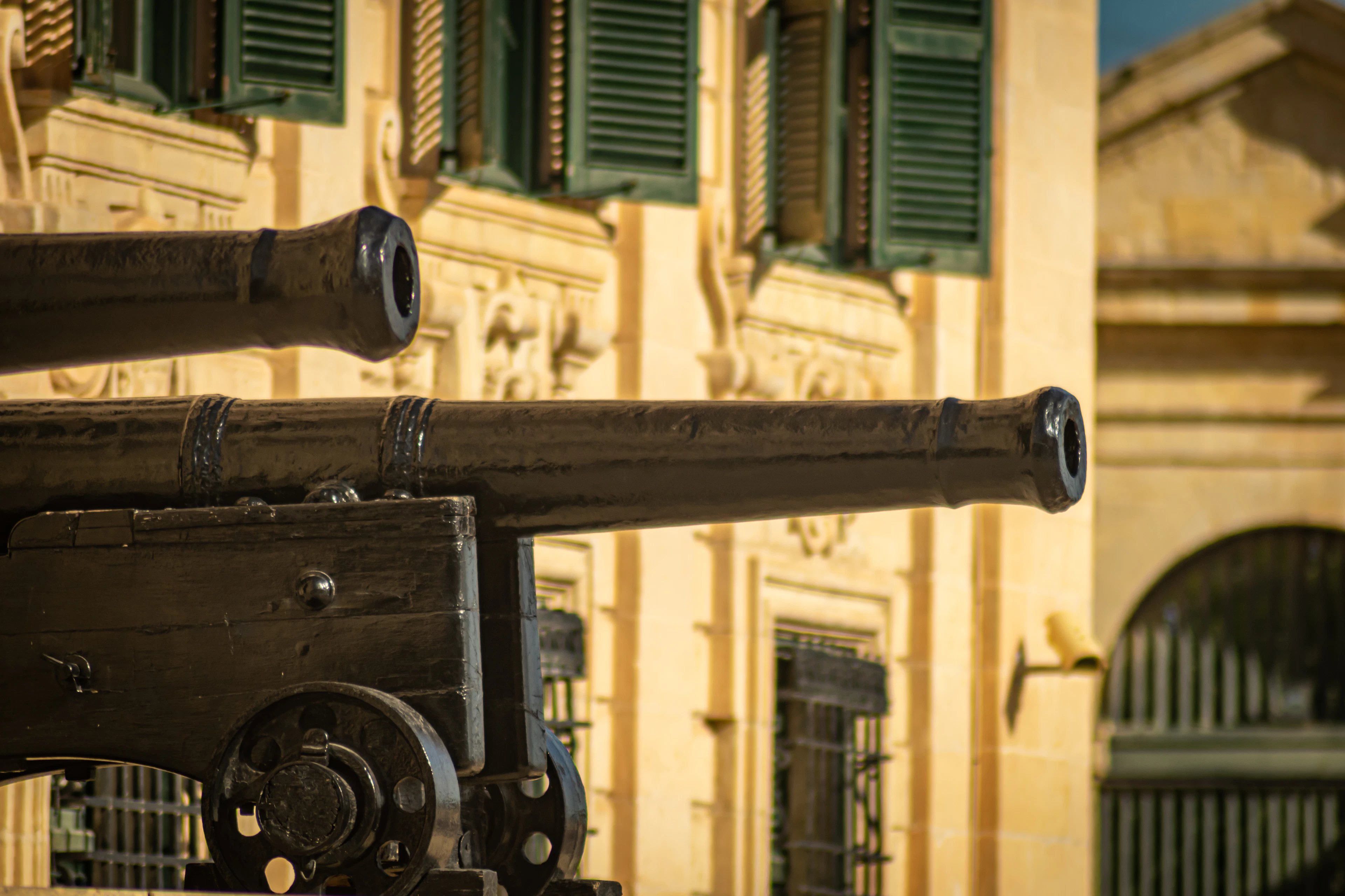 The bronze cannon of the Saluting Battery at Valletta's Upper Barrakka Gardens, green shutters on the wall behind