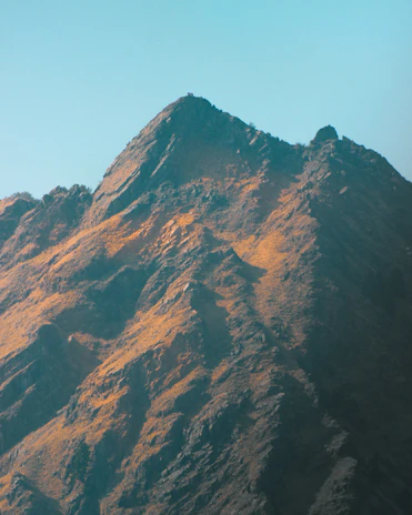 A rugged mountain peak at dawn with soft light highlighting its sharp edges, symbolizing strength and endurance.