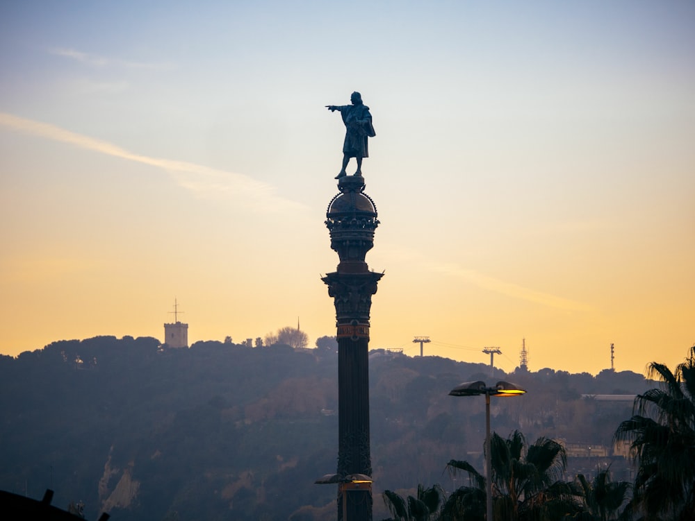 a statue of a person on a tower with a city in the background