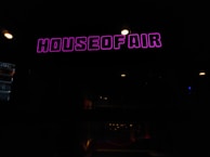 A dimly lit interior with a prominent neon sign reading 'House of Air' in bright purple letters. The ceiling has small, round spotlights providing minimal illumination.