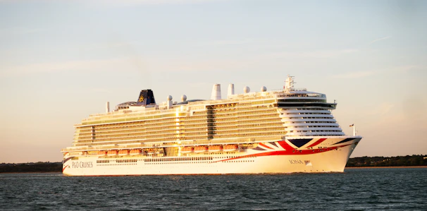 A sleek luxury cruise ship sailing under a vibrant sunset sky on calm waters.