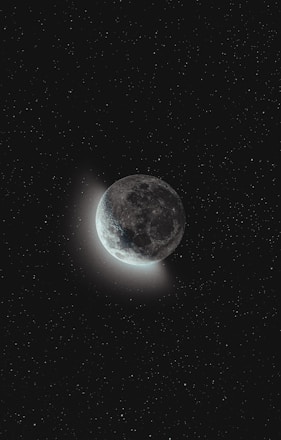A celestial scene features the moon partially illuminated against a vast, starry night sky. The surface of the moon reveals craters and a subtle glow emanates from its lit side, creating a serene and captivating contrast with the surrounding darkness.