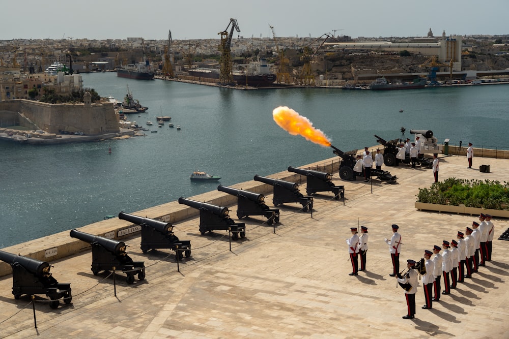 a group of people standing on a dock with cannons and a fire