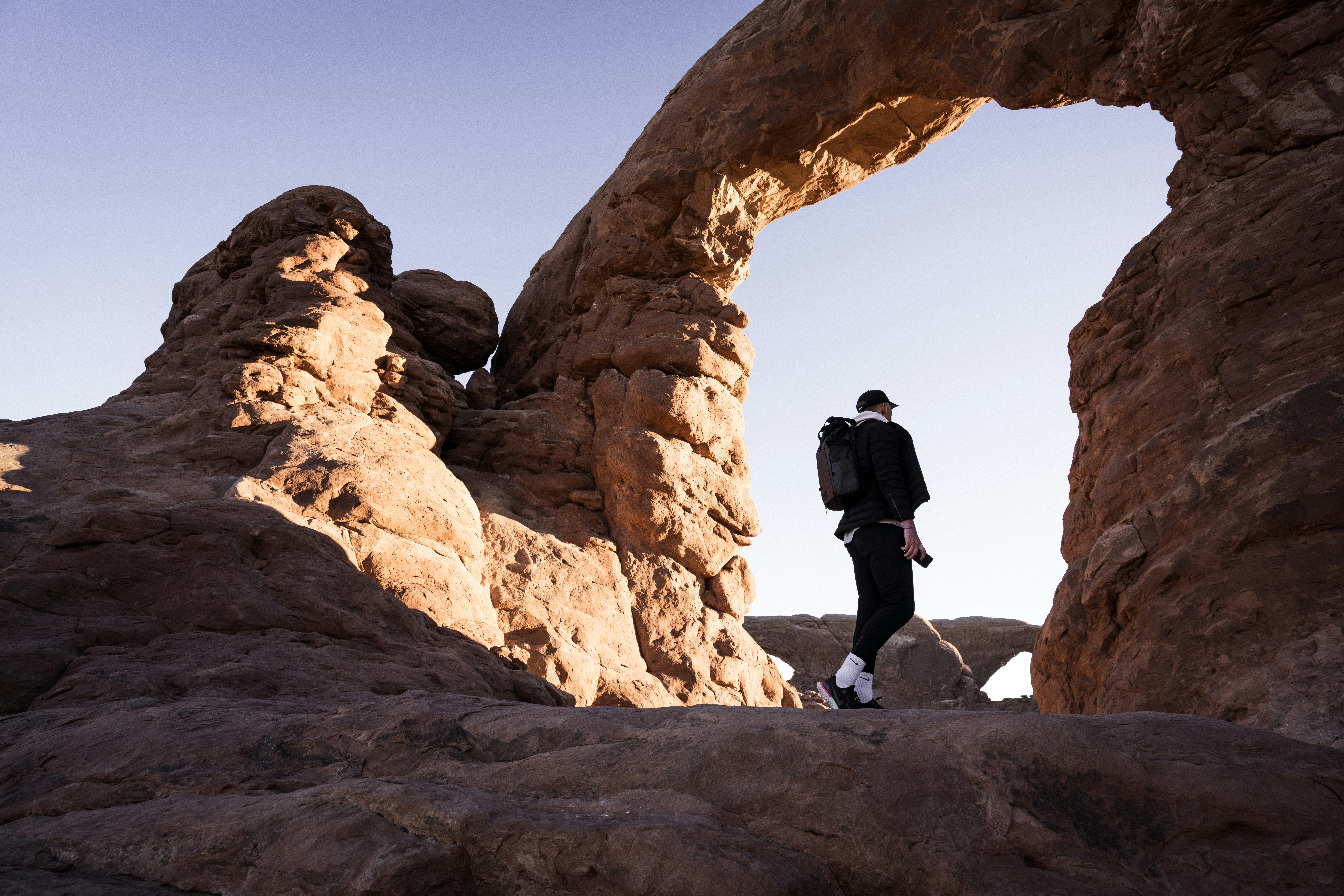 a man walking through a rock formation, Hiking at golden hour in Arches National Park in Utah